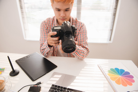 Handsome male graphic designer looking at pictures in digital camera at officeの写真素材