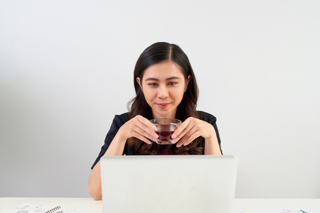 Young woman taking a tea break as she sits at a table working on a laptop computer, の写真素材