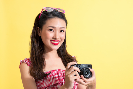 Portrait of a beautiful young asian woman on yellow background with a camera in  handsの写真素材