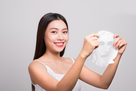 Beautiful asian woman applying paper sheet mask on her face white background.の写真素材