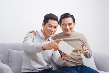 Two male friends playing game on smartphone sitting on sofa at homeの写真素材
