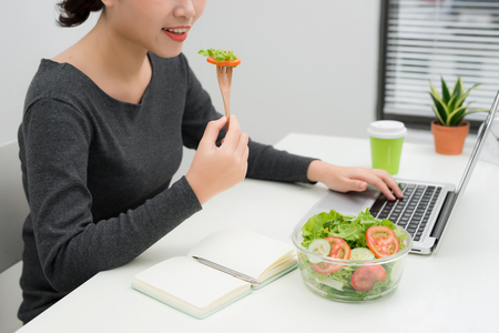 Young woman eating salad while working at desk. Weight loss conceptの写真素材