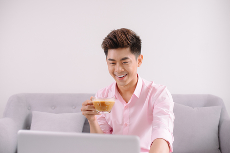Handsome asian businessman smiling while working with a laptop at homeの写真素材