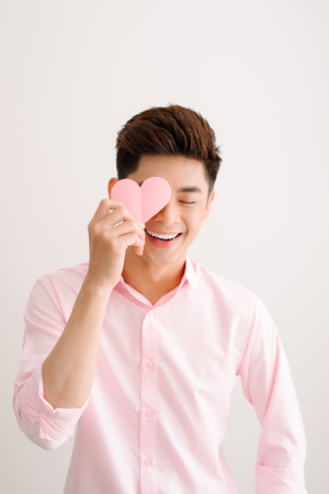 Handsome asian man holding pink heart paper posing on gray backgroundの写真素材
