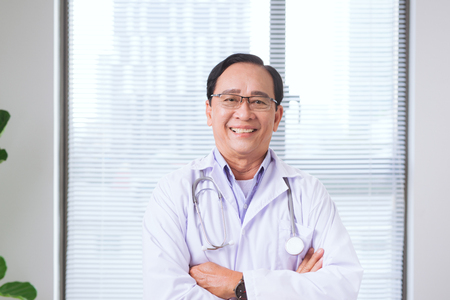 Portrait of senior doctor standing in medical officeの写真素材