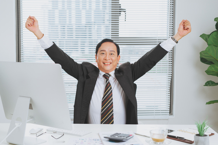 Happy mature businessman in suit celebrating unbelievable business success, raising hands.の写真素材