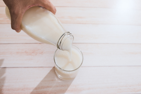 Milk is poured into a glass on a wooden tableの写真素材