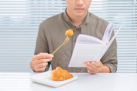 Asian man reading a book during eating breakfast in the morningの写真素材