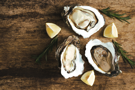 fresh just opened oysters and slice of lemon on rustic wooden background