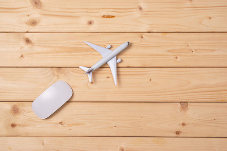 Online travel booking concept. Airplane model and computer mouse on wooden background.の写真素材