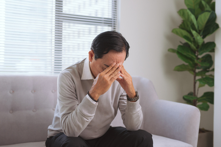Senior man having headache while sitting on couch at home.の写真素材