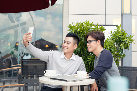 Two men are taking a selfie with a cellphoneの写真素材