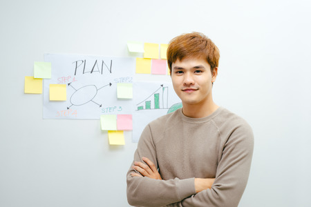 Young Asian man stands in front of his financial plan in the roomの写真素材