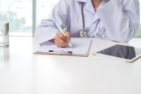 Close up on asian female doctor hands writing something on clipboardの写真素材