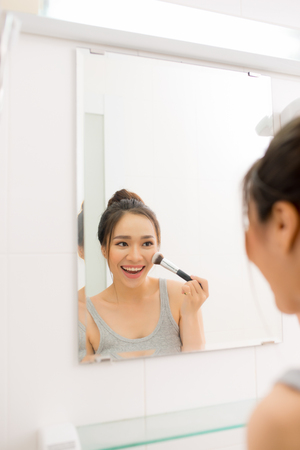 Beautiful woman applying makeup blusher in her bathroomの写真素材