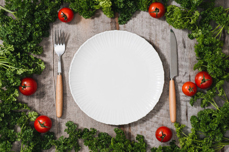 Fresh seasonal organic vegetables,ingredients cutlery and kitchen checked napkin on light rustic background, top view, frame. Healthy eating or clean food concept.の写真素材