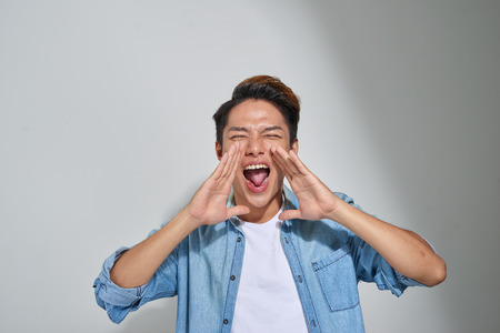 Young man shouting with hands cupped to his mouthの写真素材
