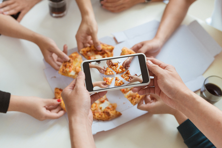 Hands taking picture of delicious pizza with smartphone.の写真素材