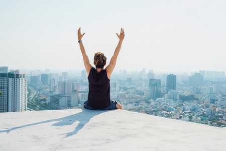 Man sitting on top roof and show hand up with blue sky background and sunshineの写真素材