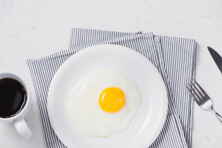 Top view of white dish with fried egg on white background.