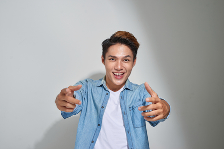 Portrait handsome young smiling man giving thumbs up pointing fingers at camera, picking you as friend isolated on grey wall background. Positive human emotion facial expression sign body languageの写真素材