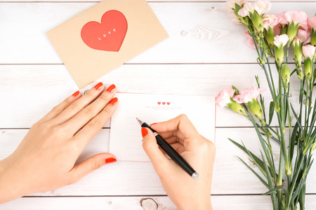 Woman writes love letter on white paper with red heart shape figures.Hand made postcard for Saint Valentines Day celebration.Send letters for your lovers & friends on 14th of Februaryの写真素材