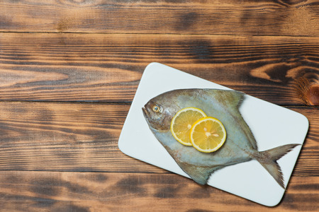 Fish dish cooking with various ingredients. Fresh raw fish decorated with lemon slices and herbs on...