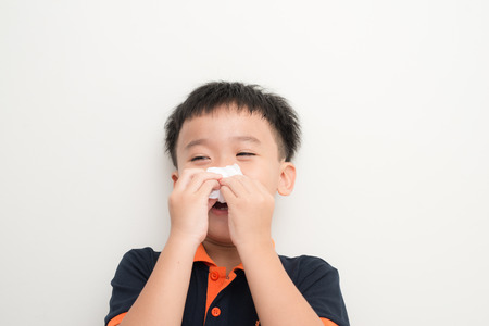 Cute little boy sneezing in tissue on white backgroundの写真素材