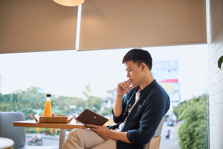 Businessman writing on notebook by cafe window, Concentrated on work, Side view of confident young man is working on notebook while sitting and writing in cafe,Age 20-30 years.の写真素材