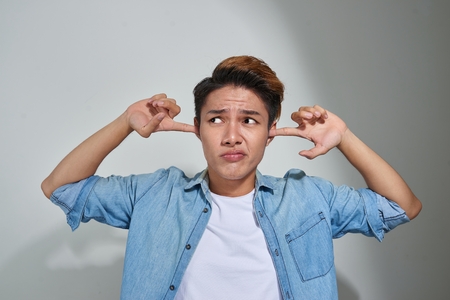 displeased man plugging ears with fingers doesn't want to listen isolated on gray wall backgroundの写真素材