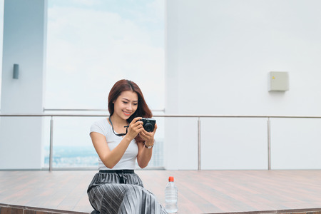 Beautiful asian woman sit at the edge of street, smiling with camera in hand, travel concept.の写真素材