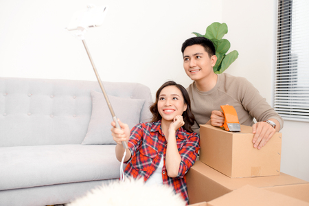 home, people, repair and real estate concept - smiling couple with big cardboard boxes moving to new place and taking smartphone selfieの写真素材
