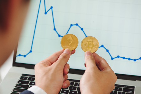Man holding physical bitcoin and ethereum cryptocurrency coins in his hands on the background of the...