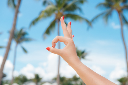Holiday, beach rest. Woman hand showing okay sign gesture, against the backdrop of summer beachの写真素材