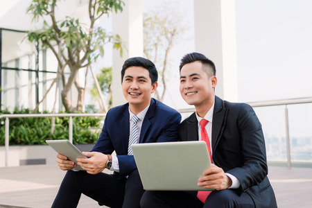 Business man in suit using laptop and business woman using the smartphone in front of the building.の写真素材