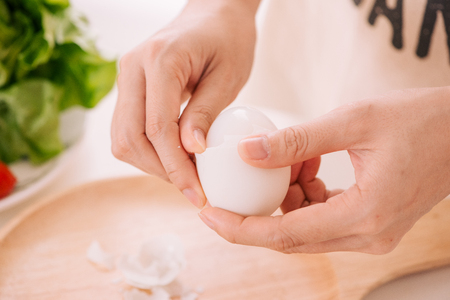 Female hands is shelling chicken eggs. The woman prepares breakfast at home. Boiled chicken eggs in wooden ware on a dark table. Vintage toningの写真素材
