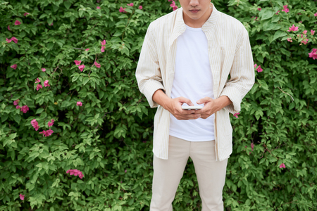 Handsome man texting on mobile phone while walking in green parkの写真素材