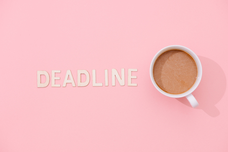 DEADLINE text with a cup of coffee with shadow on pink background.の写真素材