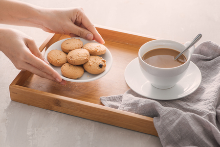 Hand putting cookies on plate into tray. Breakfast concept with coffeeの写真素材