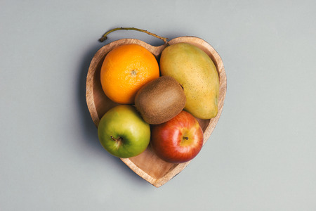 Orange, mango, apple and kiwi in a wooden heart-shaped plateの写真素材