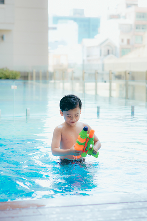 Little boy shooting with water gun in the poolの写真素材