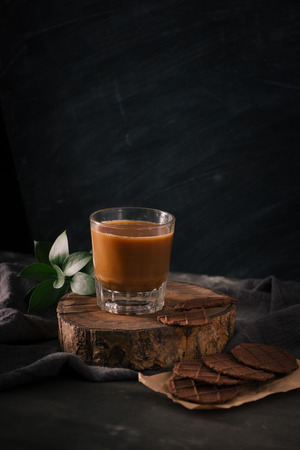 Assorted cookies in brown paper and glass of coffee with milk on dark background.の写真素材