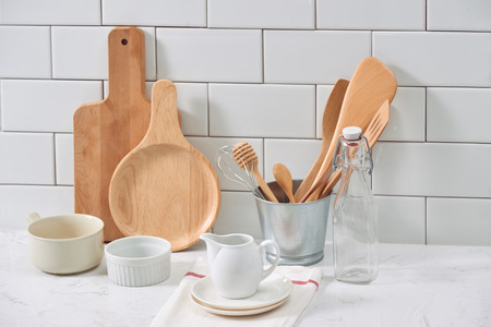 Simple rustic kitchenware against white wooden wall: rough ceramic pot with wooden cooking utensil...