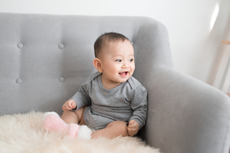 Baby girl is smiling and sitting on sofa in jumpsuitの写真素材