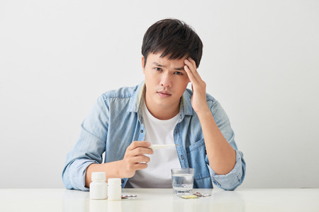 Sick young man looks at a thermometer