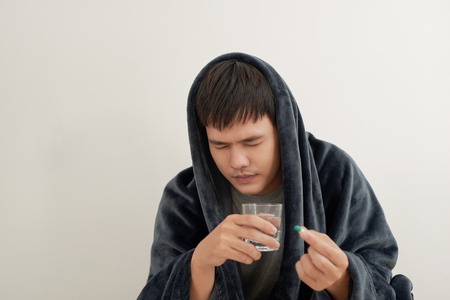 A young man is sick with flu, lies at home under a blanket, takes a pillの写真素材