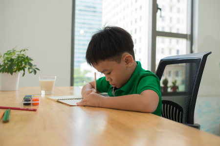 Cute smiling boy doing homework, coloring pages, writing and painting . Children paint. Kids draw. Preschooler with books in the library. Colorful pencils and paper on a desk. Creative boy.の写真素材