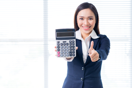 Smiling businesswoman portrait in office standing and holding calculatorの写真素材