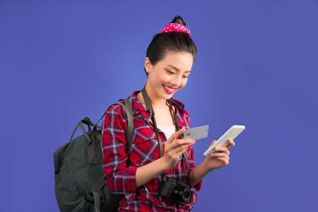 Happy young asian woman holding credit card and smartphone standing over blue.の写真素材