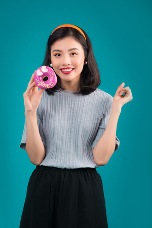 Smiling lovely asian woman dressed in pin-up style dress holding donut over blue.の写真素材